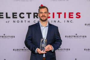 a person in a dark suit holding an award stands in front of a backdrop with the text 'electricities of north carolina, inc.'